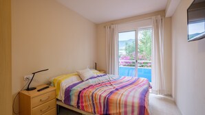A bedroom with a bed, a nightstand, a dresser, a window with curtains, and a view of a balcony with flowers. - Apartment "Merida" with Shared Pool, Terrace and Wi-Fi (ALCANAR)