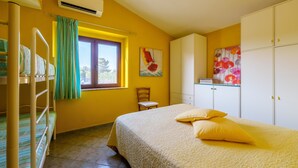 Ein Zimmer mit Etagenbetten, einem Bett mit gelber Bettwäsche, einem Fenster mit Vorhängen, einem Stuhl und einem Kleiderschrank.