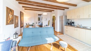 Un espacio habitable moderno con sofá, vigas de madera, cocina con armarios de colores claros y obras de arte en las paredes.