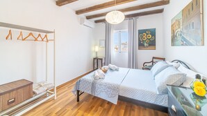 Un dormitorio con techo de madera, una cama con colcha estampada, una mesita de noche con un jarrón y un cuadro en la pared.