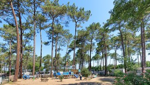 A campground with tall pine trees, a children's play area, and RVs. - Holiday Apartment "Mobile-home Alain" with Garden & Terrace (Saint-Julien-en-Born)