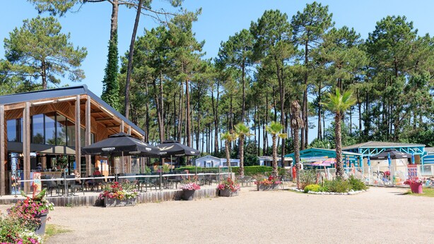 A restaurant with outdoor seating, surrounded by tall pine trees. - Holiday Apartment "Mobile-home Alain" with Garden & Terrace (Saint-Julien-en-Born)