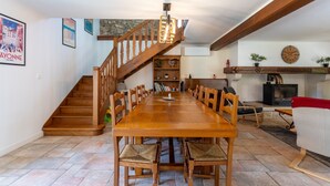A dining area with a wooden table and chairs, a staircase, a fireplace, and a clock on the wall. - Holiday Home "Maison Elixondoa" with Mountain View, Wi-Fi (Pagolle)