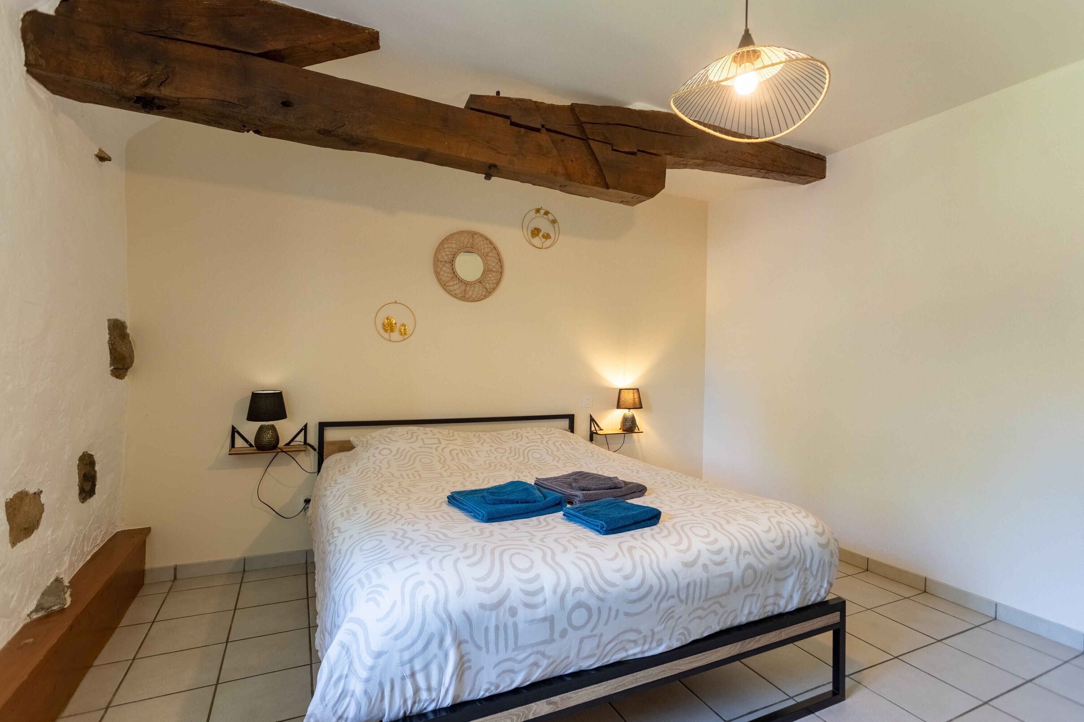 A bedroom with a bed, wooden beams, wall decor, and a lamp.