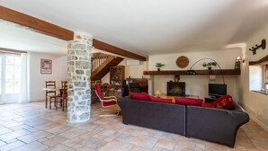 A spacious living area with a stone pillar, wooden beams, a sofa, a fireplace, and a television. - Holiday Home "Maison Elixondoa" with Mountain View, Wi-Fi (Pagolle)