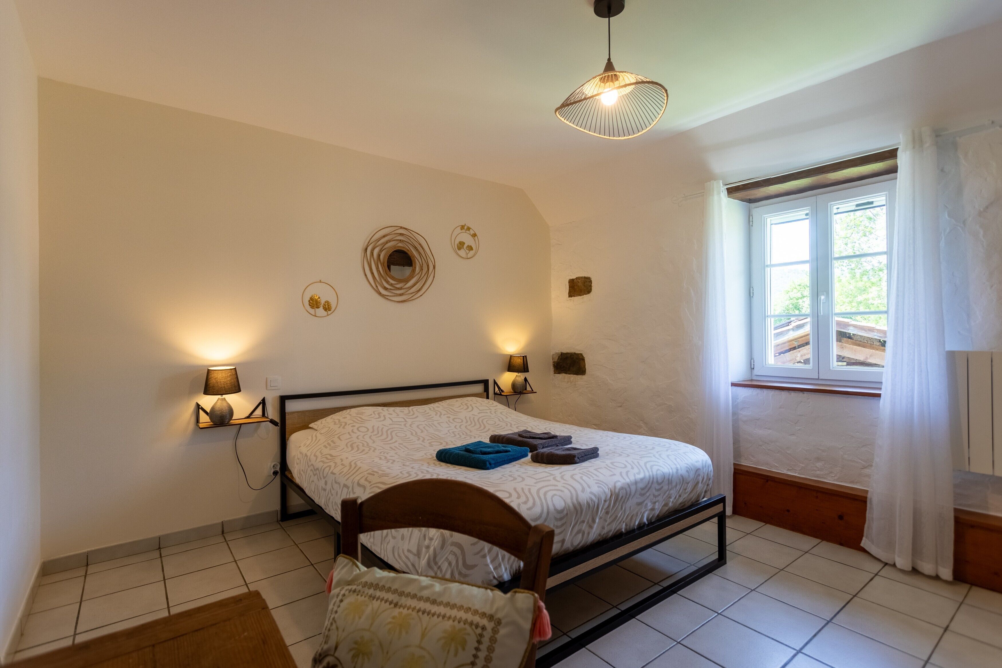 Un dormitorio con cama, lámparas de noche, una ventana con cortinas, cabecera de madera y decoración en la pared.