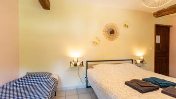 A room with two beds, a wooden ceiling beam, wall-mounted lamps, and a door.