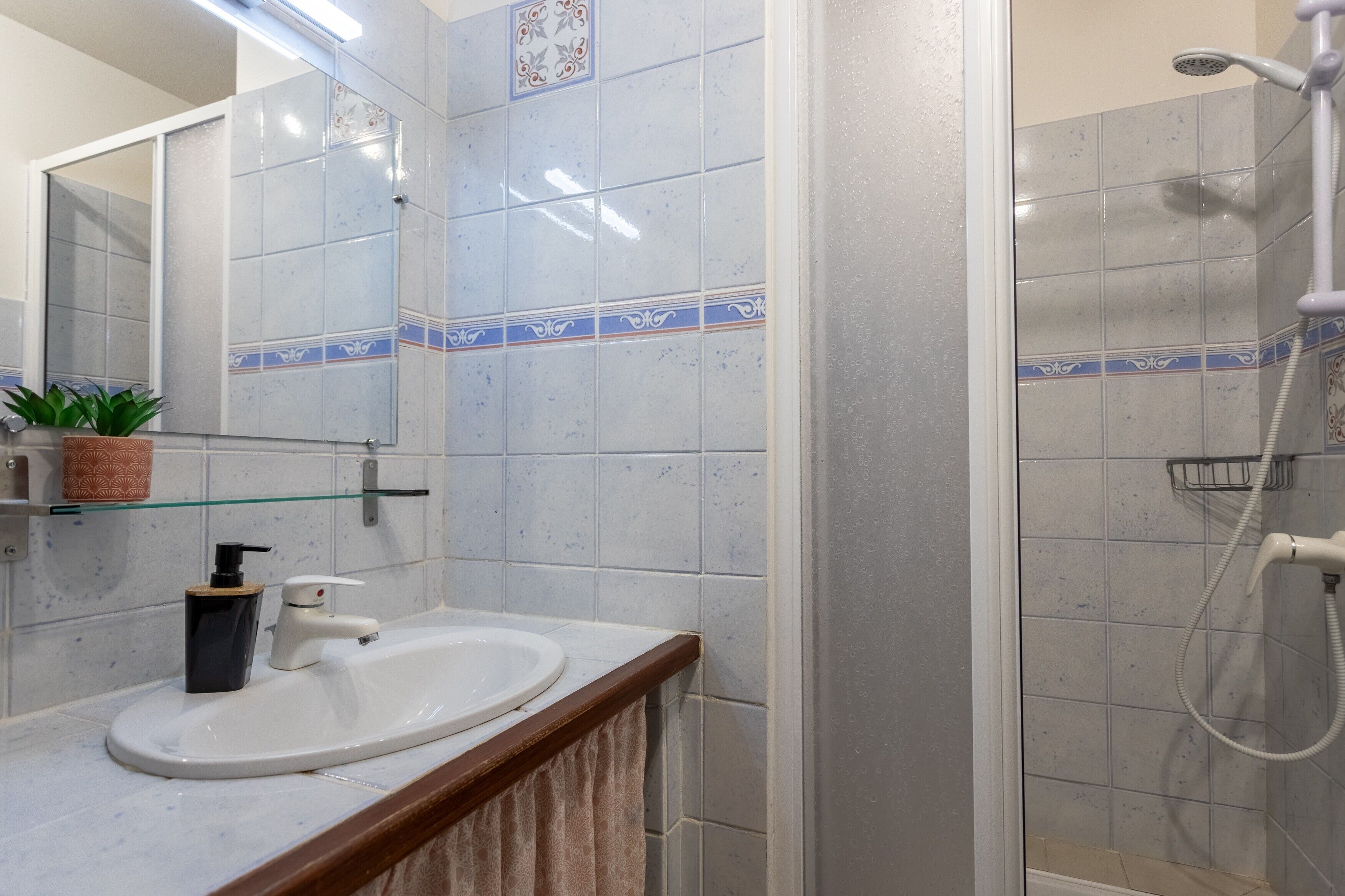 Un bagno con lavandino, specchio, doccia e pareti piastrellate.