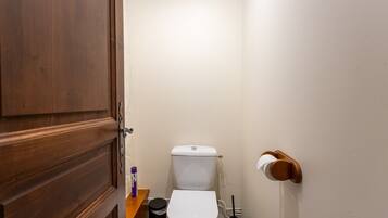 Une petite salle de bain avec une porte en bois, des toilettes blanches, une poubelle noire et un porte-rouleau de papier toilette.