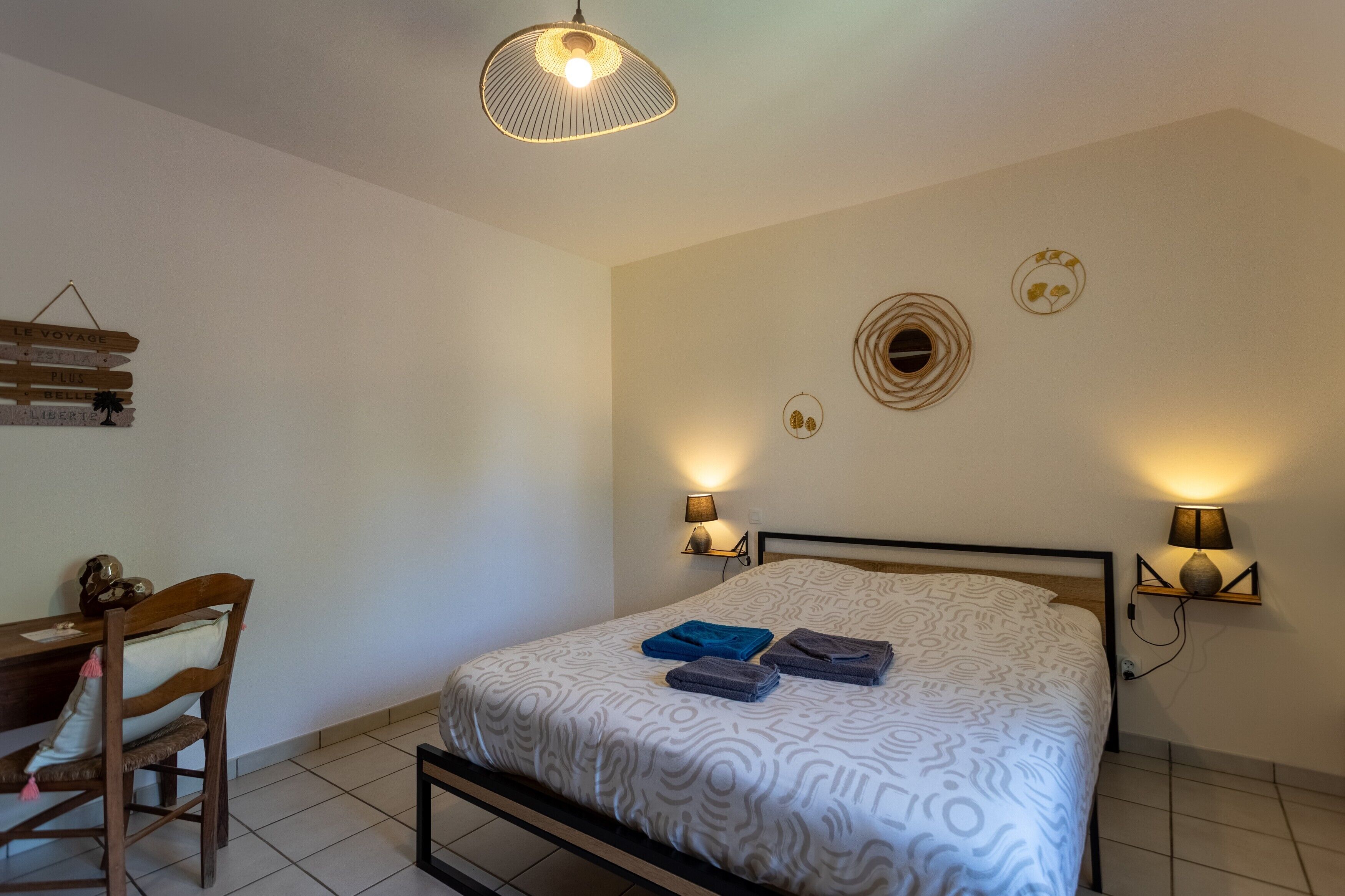 Een slaapkamer met een bed, bedlampjes, een bureau en een stoel.
