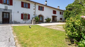 A two-story building with red shutters, a stone entrance, and a small statue in the front yard. - Holiday Home "Maison Elixondoa" with Mountain View, Wi-Fi (Pagolle)