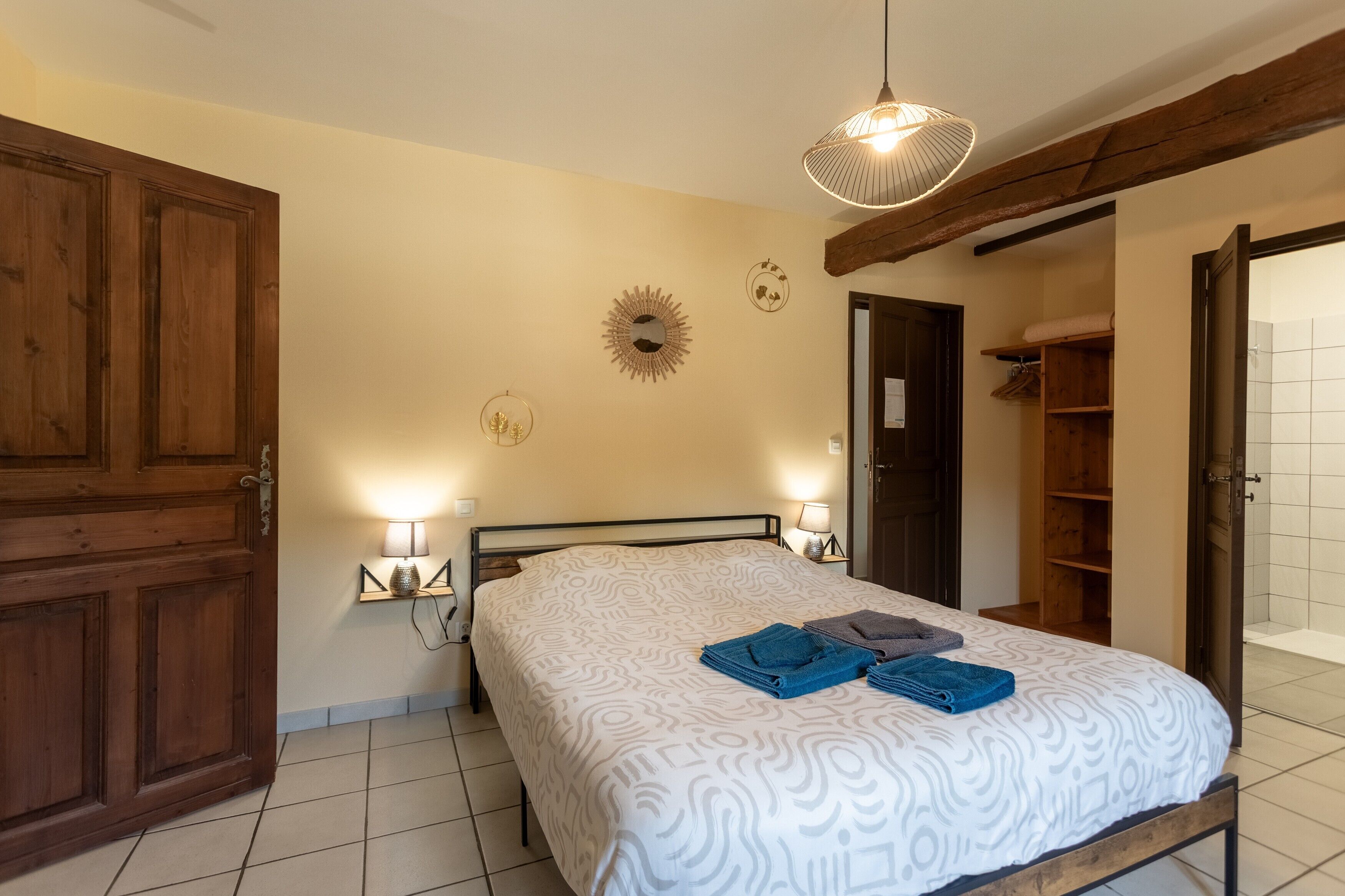 Ein Schlafzimmer mit Bett, Nachttischlampen, einem Holzschrank, einem Spiegel und einer Tür zu einem Badezimmer.