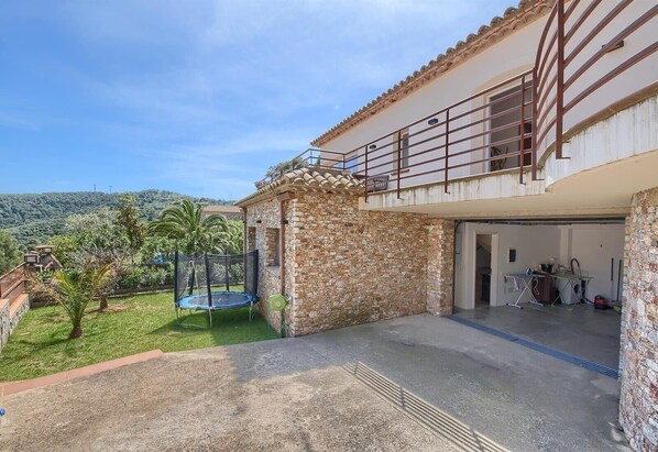 A house with a stone exterior, a trampoline in the backyard, and a garage.