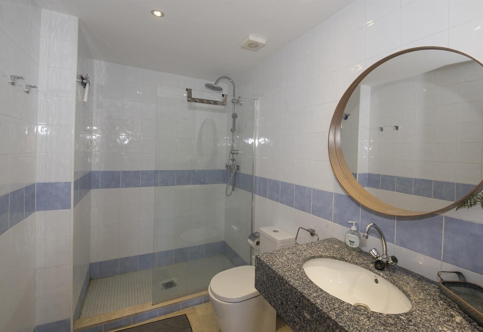 A bathroom with a glass-enclosed shower, a sink with a granite countertop, and a mirror with a wooden frame.
