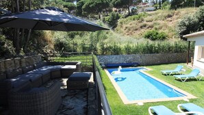 Una piscina con sillas de descanso, una zona de estar cubierta y un muro de piedra.