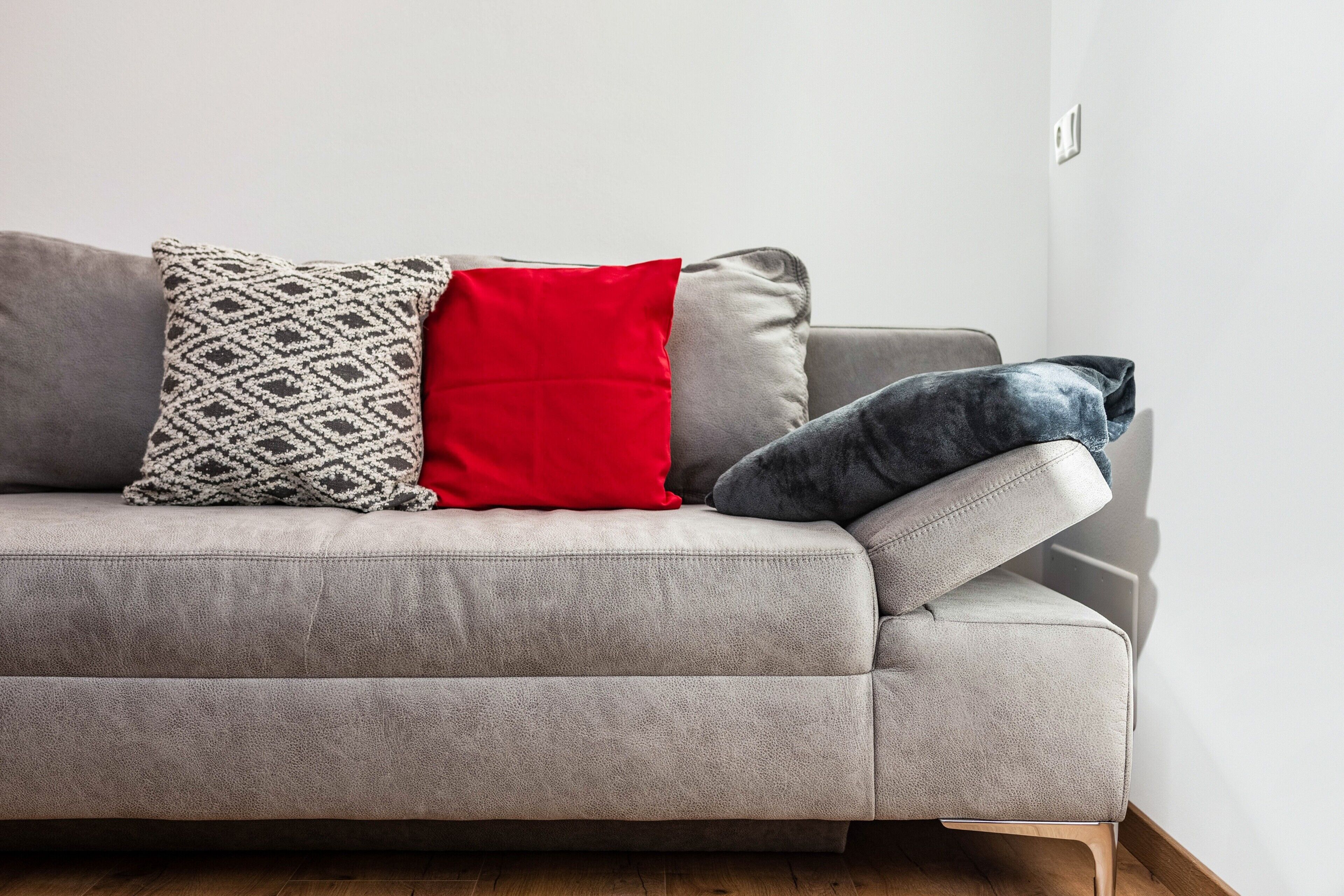 A grey sofa with patterned and solid pillows, a wooden floor, and a white wall.