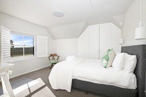 Relax in this serene bedroom with a large bed, white wardrobe, and comfortable chair.