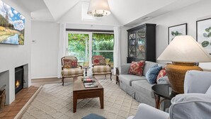 Un salon avec une cheminée, un canapé, deux fauteuils, une table basse et une lampe.