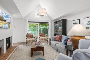 Cozy living room with a fireplace, comfortable seating area, and large windows offering a view of the surrounding greenery.