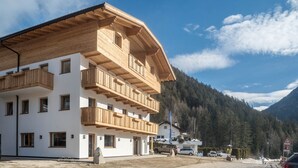 Un edificio de varios pisos con balcones de madera, cielo despejado y montañas al fondo.