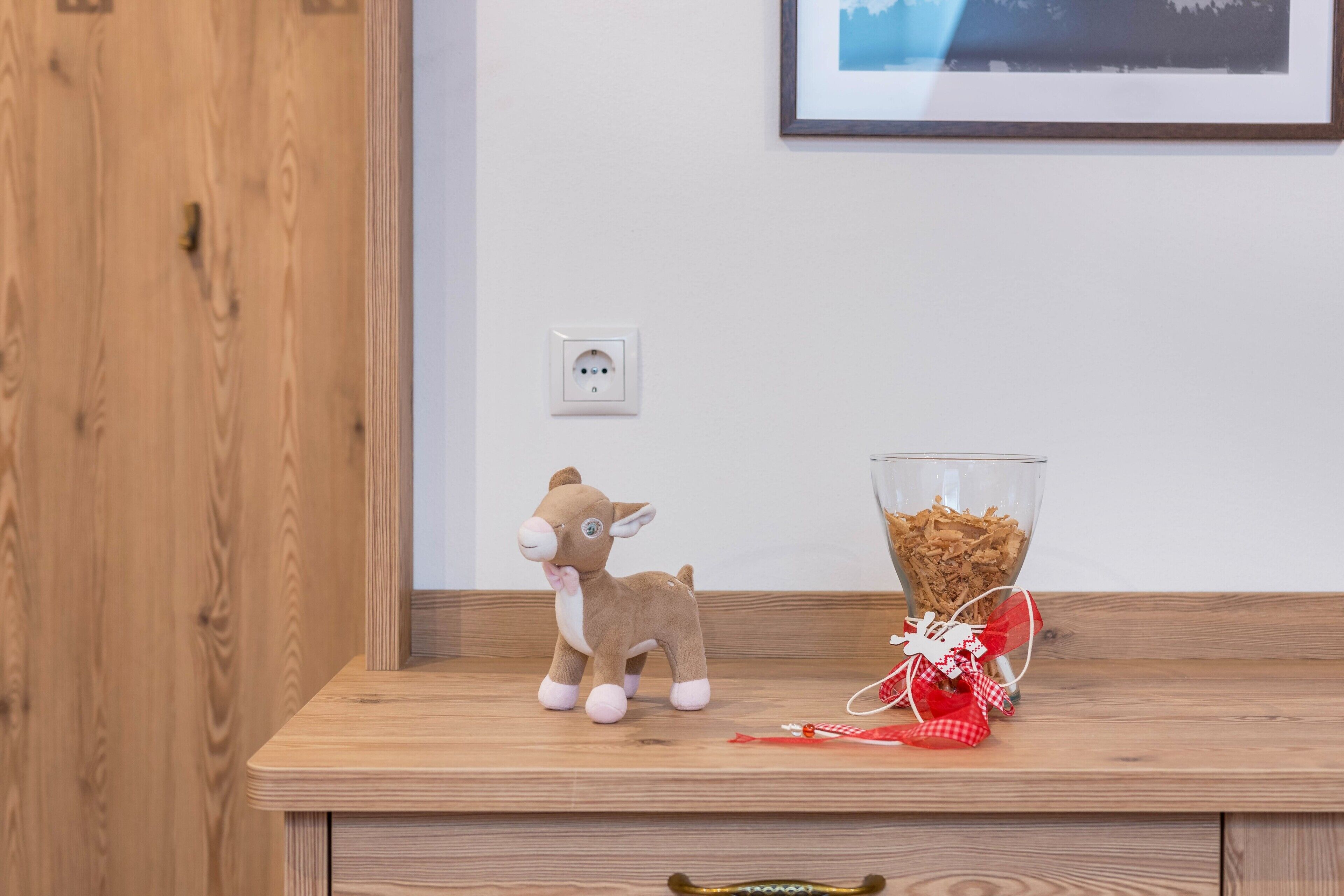 A wooden shelf with a plush toy, a glass bowl with cereal, and a red and white gift-wrapped item.