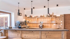 Zona de bar con estantes de madera, taburetes y una máquina de café.
