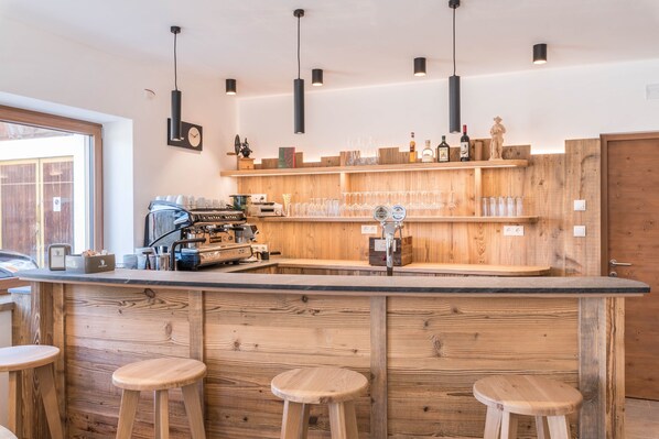 Un espace bar avec des étagères en bois, des tabourets et une machine à café.