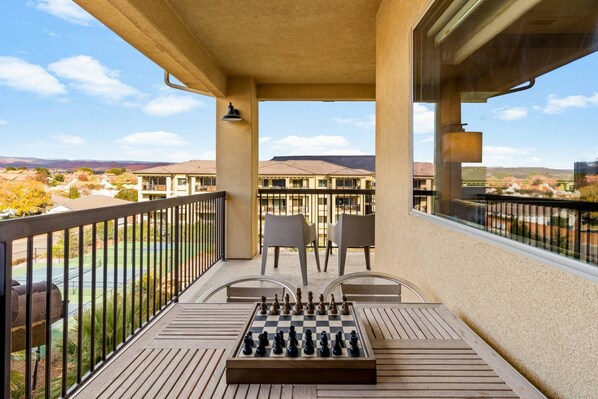 A balcony with a chessboard, two chairs, and a view of a residential area.