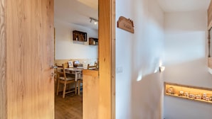 A wooden interior with a kitchen area, a dining table, and a shelf with jars.