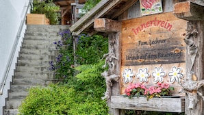 A wooden sign with 'Innertrein' and 'Fam. Lechner' written on it, a wooden staircase, and a flower box with pink flowers.