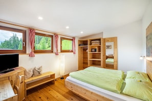 Un dormitorio con cama de madera, televisor, banca y armario.