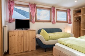 Quarto com cama, televisão, guarda-roupa de madeira e janela com cortinas.