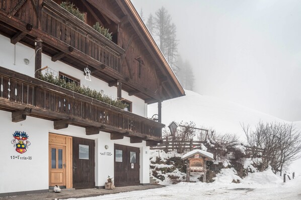 Una cabaña tradicional con balcones de madera, fachada blanca y un paisaje cubierto de nieve.