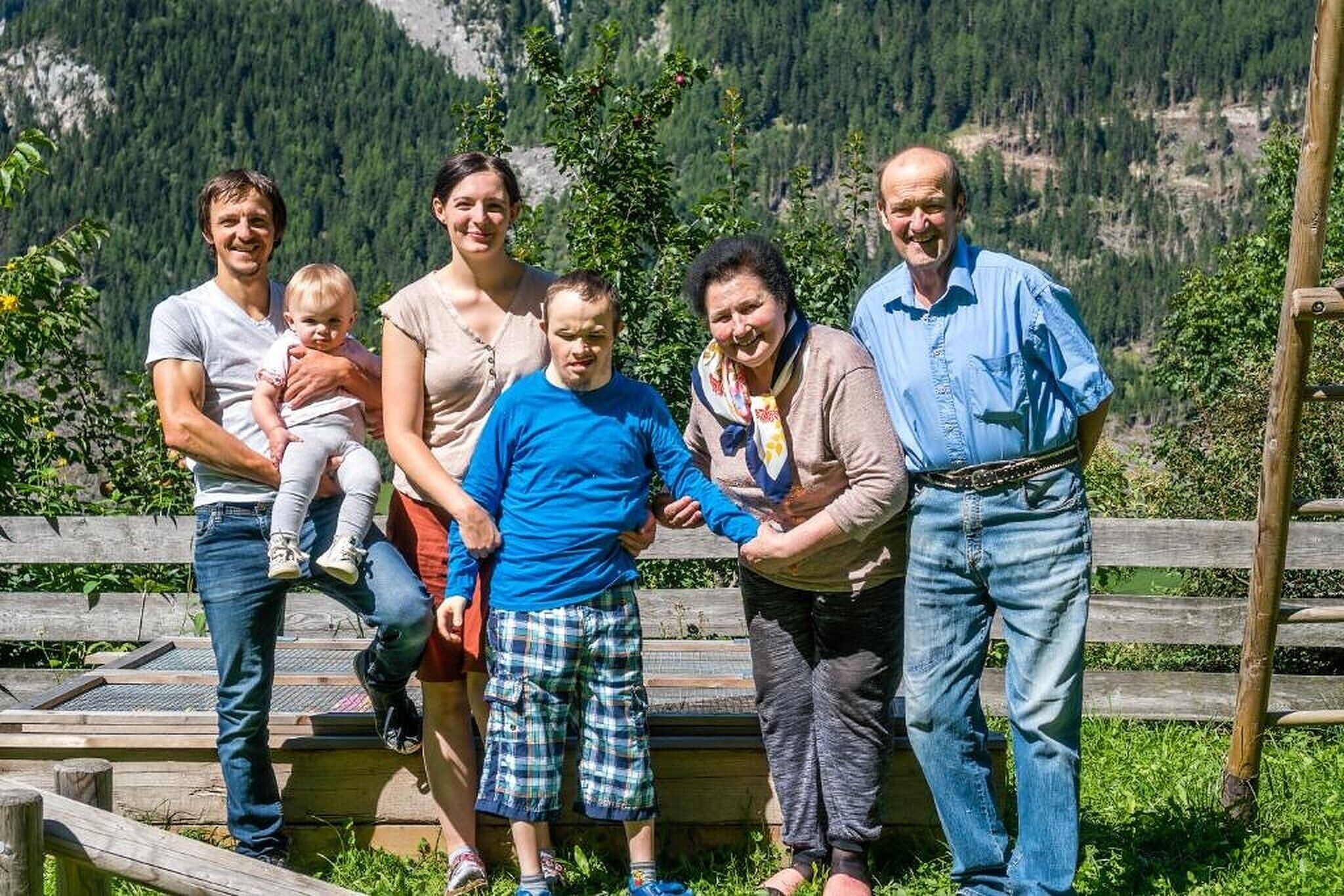 Eine Gruppe von Menschen steht auf einer Holzplattform vor einer Berglandschaft.