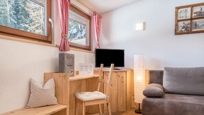 Una habitación acogedora con un escritorio de madera, un sofá gris, una ventana con cortinas a cuadros blancos y rojos y un cuadro en la pared.