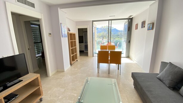 Uma sala de estar moderna com televisão de tela plana, mesa de centro de vidro, sofá e área de jantar com mesa e cadeiras.