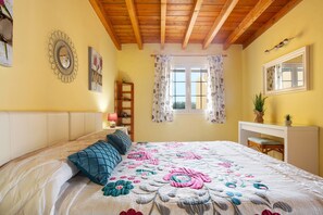 Quarto com cama, mesa de cabeceira, espelho, janela com cortinas e teto de madeira.