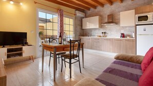 A modern kitchen with a dining area, wooden ceiling beams, and a television.