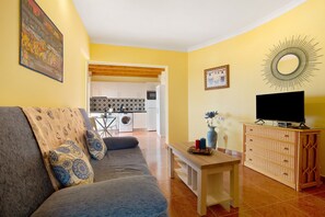 A living room with a sofa, a TV on a wooden cabinet, a dining table, and a kitchen in the background. - Vacation Home "Casa Paco 2" with Sea View, Private Balcony & Shared Pool (Costa Calma)