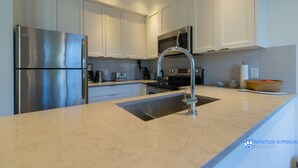 A modern kitchen with stainless steel appliances, white cabinetry, and a granite countertop. - Fully renovated condominium in Stoney Creek Northstar. Village location, Pool, Hot Tub, Free Parking (Whistler)