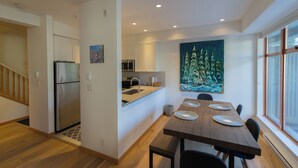 A modern kitchen with stainless steel appliances, a dining area with a wooden table and chairs, and a large window providing natural light. - Fully renovated condominium in Stoney Creek Northstar. Village location, Pool, Hot Tub, Free Parking (Whistler)