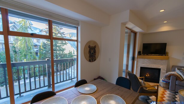 A spacious living area with a fireplace, a large window with a view of the outdoors, and a dining table with placemats. - Fully renovated condominium in Stoney Creek Northstar. Village location, Pool, Hot Tub, Free Parking (Whistler)
