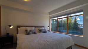 A bedroom with a large bed, two bedside lamps, and a window with a view of trees and a house. - Fully renovated condominium in Stoney Creek Northstar. Village location, Pool, Hot Tub, Free Parking (Whistler)