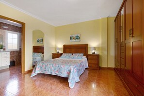 Ein Schlafzimmer mit einem Bett, Nachttischen, einem Holzschrank und einem durch einen Bogen erreichbaren Badezimmer.