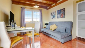 A room with a wooden ceiling, a grey sofa, a white table with chairs, a window with curtains, and artwork on the wall. - Vacation Home "Casa Paco 3" with Sea View, Private Terrace & Shared Pool (Costa Calma)