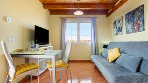 A room with a TV, a sofa, a dining table, chairs, and artwork on the walls. - Vacation Home "Casa Paco 3" with Sea View, Private Terrace & Shared Pool (Costa Calma)