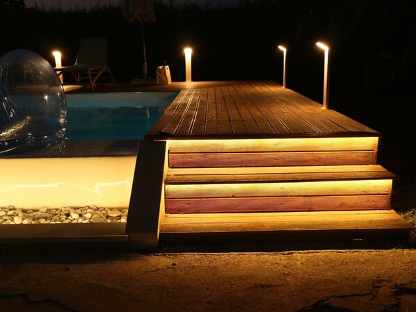 A wooden deck leading to a pool with a clear water surface, surrounded by a dark environment.
