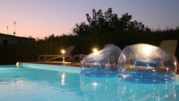 Una piscina con agua cristalina, dos estructuras en forma de cúpula transparente y sillas de descanso.