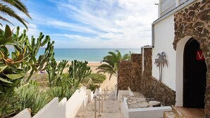 Un sendero que conduce a una playa, con vista al océano, un muro de piedra y una puerta con un cartel con la letra 'V'.
