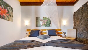 Una cama con dosel, dos lámparas fijadas a la pared, un cuadro de flores y una pared de piedra.